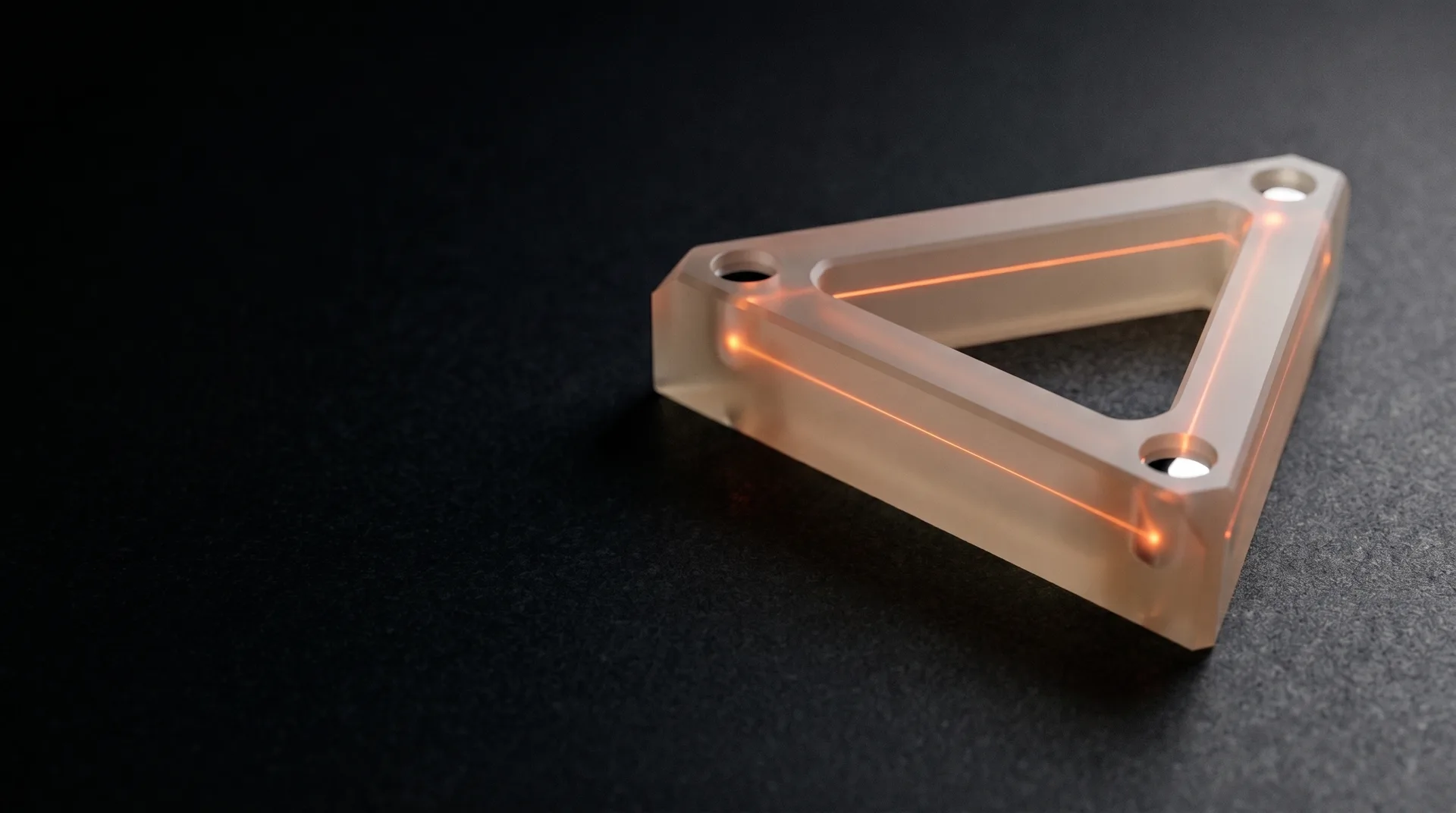 A hollow triangular ring laser gyroscope cavity block of pale glass-ceramic on a black granite table with a thin orange laser beam tracing the three bores